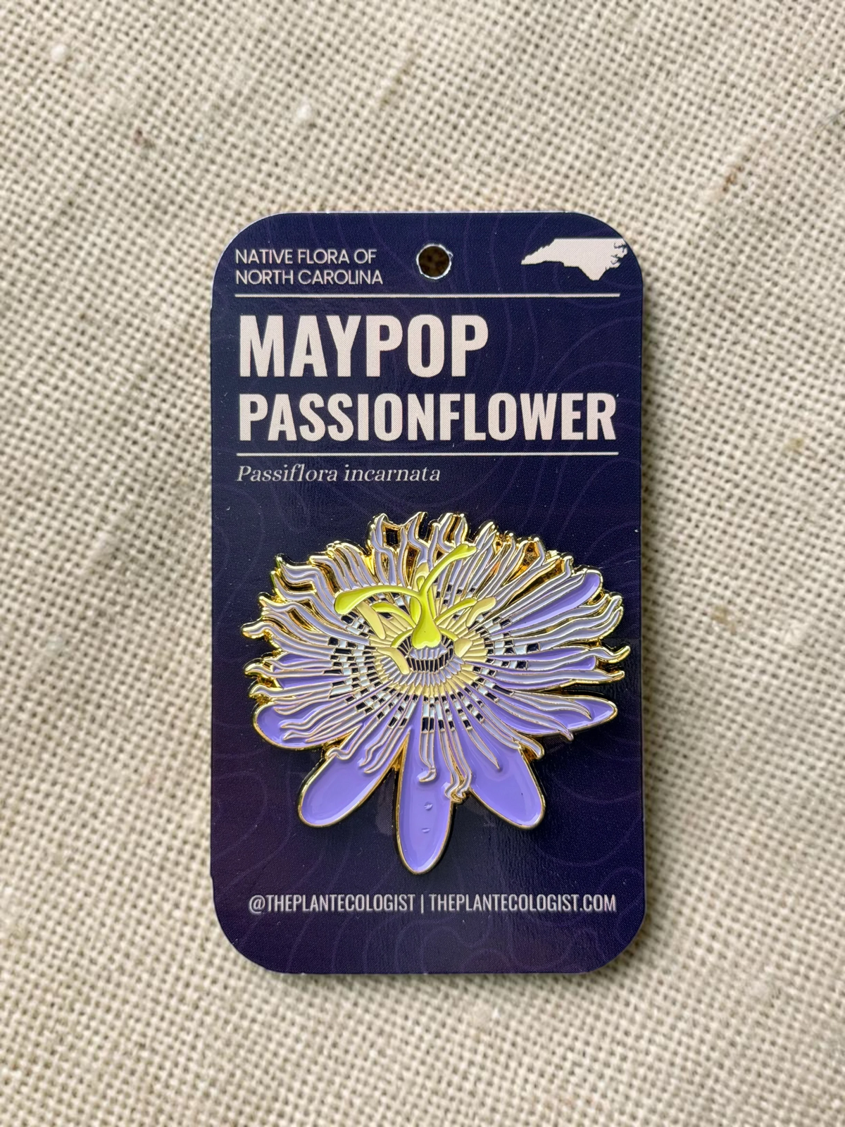 The Plant Ecologist Maypop passion flower enamel pin featuring purple and yellow details on a branded display card.