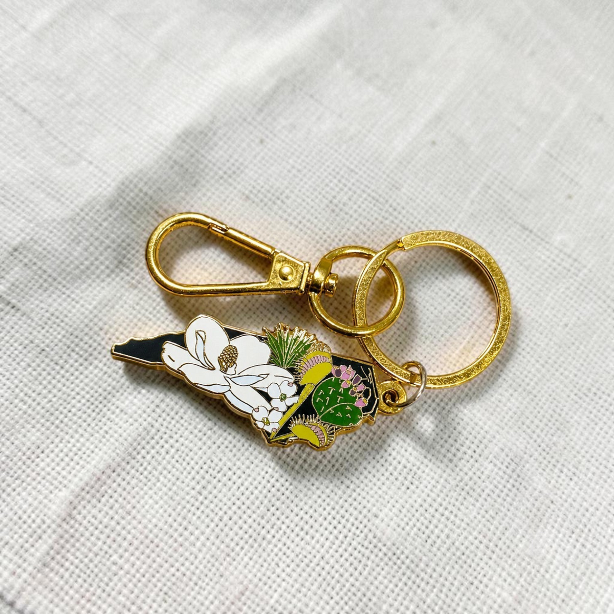 The Plant Ecologist North Carolina state shaped enamel keychain featuring native plants on a stone surface.