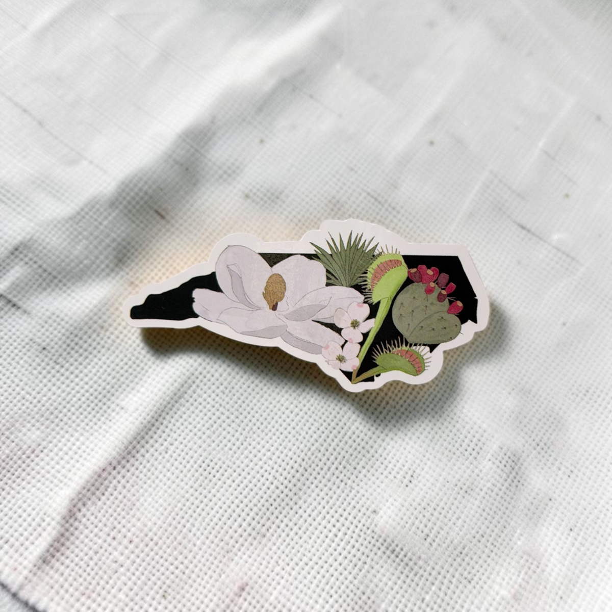 The Plant Ecologist die-cut sticker featuring a black North Carolina state silhouette with native plants and flowers