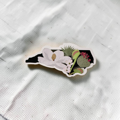 The Plant Ecologist die-cut sticker featuring a black North Carolina state silhouette with native plants and flowers