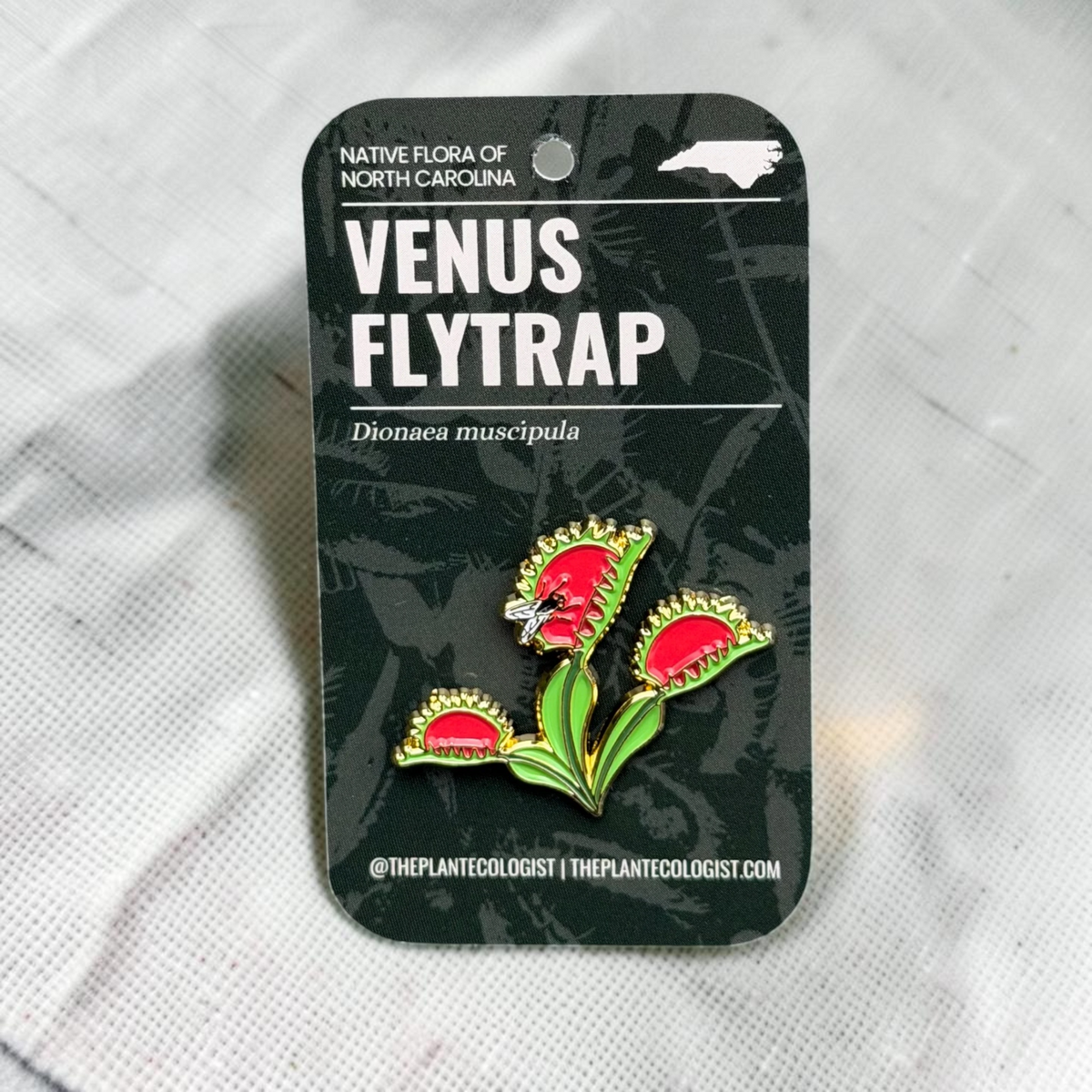 The Plant Ecologist Venus Flytrap enamel pin on a black backing card featuring North Carolina native flora text.
