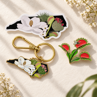 The Plant Ecologist Venus Flytrap pin, NC native plants keychain, and die-cut sticker set on a textured fabric.